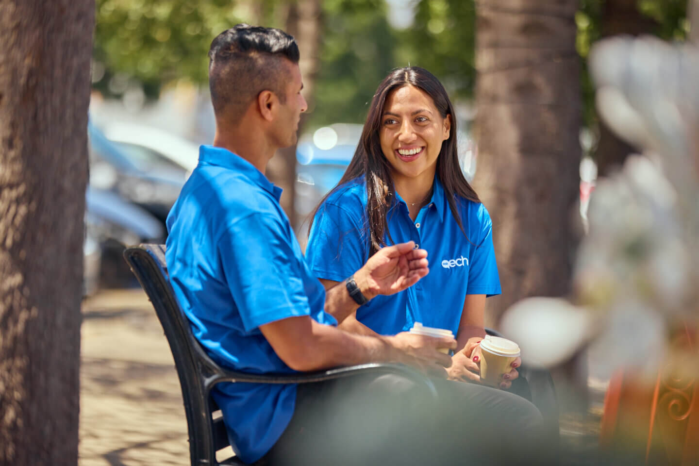 wo ECH staff members wearing blue polo shirts are sitting outdoors, smiling and having a conversation.