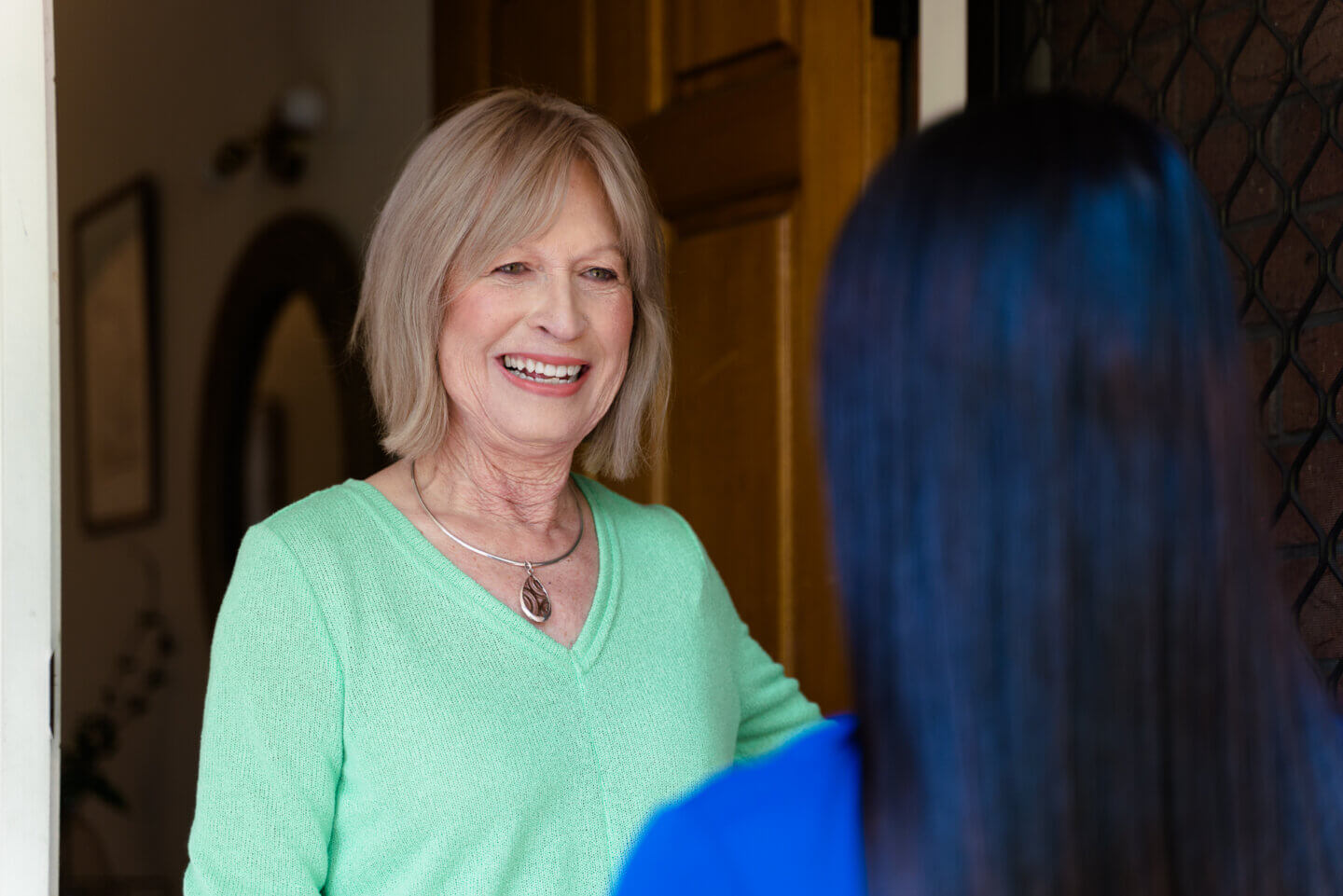 A smiling older woman wearing a light green sweater, engaging in conversation with someone from ECH's Support At Home team.