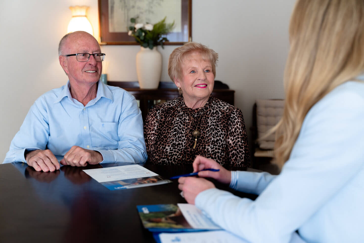 An elderly man and woman smile at an ECH caregiver across a table discussing Support At Home options